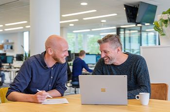 Twee collega's bespreken projectdetails met een laptop in een moderne kantoorruimte, gericht op e-commerce en productdata.